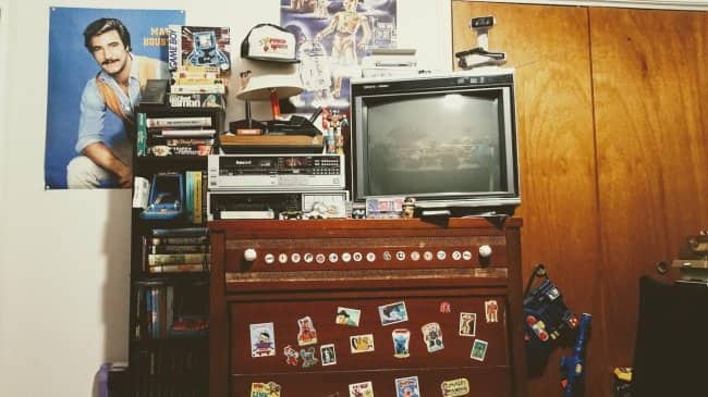Dresser with a CRT TV, VCR, stickers, and a Magnum P.I. poster on the wall.