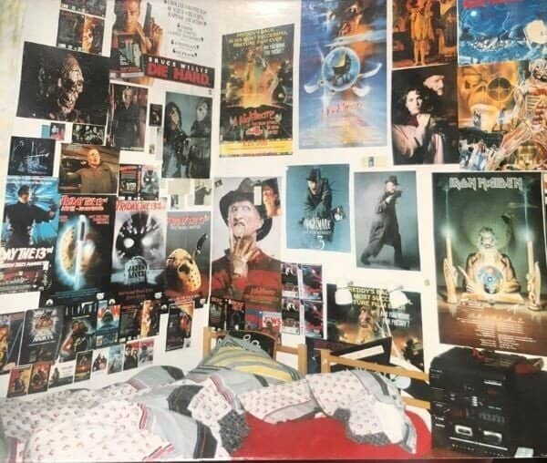 Bedroom wall packed with horror movie and Iron Maiden posters above an unmade bed.