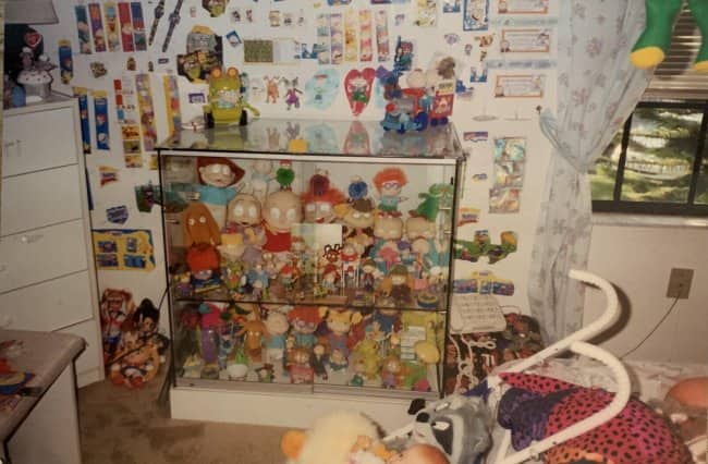Glass display cabinet packed with Rugrats toys in a pastel 90s bedroom.