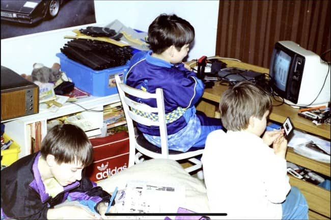 Three kids playing video games and a handheld console in a cluttered bedroom.