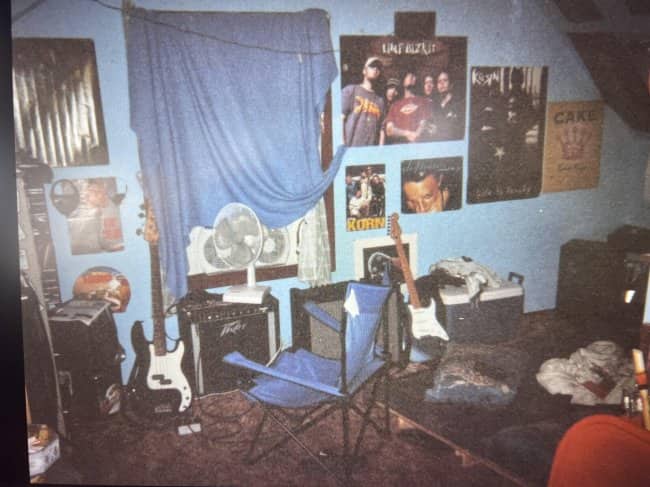 Attic bedroom with Limp Bizkit and Korn posters, guitars, an amp, and a camp chair.