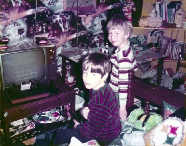 Two boys beside an old TV and console, with Star Wars wallpaper behind them.