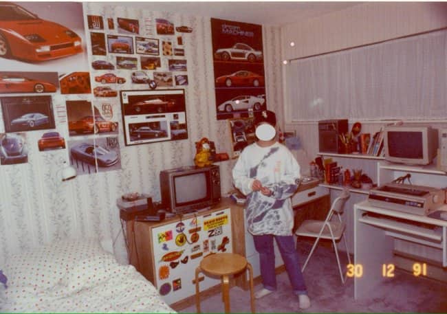 Kid in a tie-dye shirt in a 1991 bedroom covered in sports car posters.