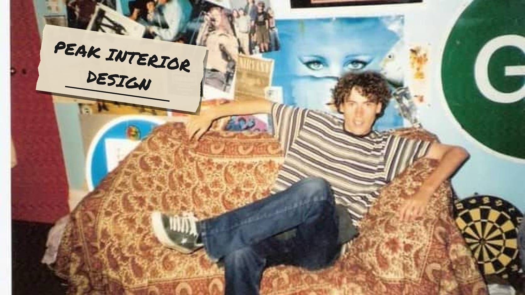 Curly haired teen lounging in a papasan chair in front of a wall covered in posters, a classic look at 90s bedrooms.