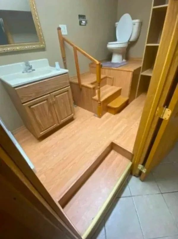 Bathroom where the toilet sits on a raised wooden stage with stairs and a railing.