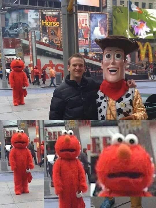 Tourist posing with Woody in Times Square while an Elmo costume stares from the background