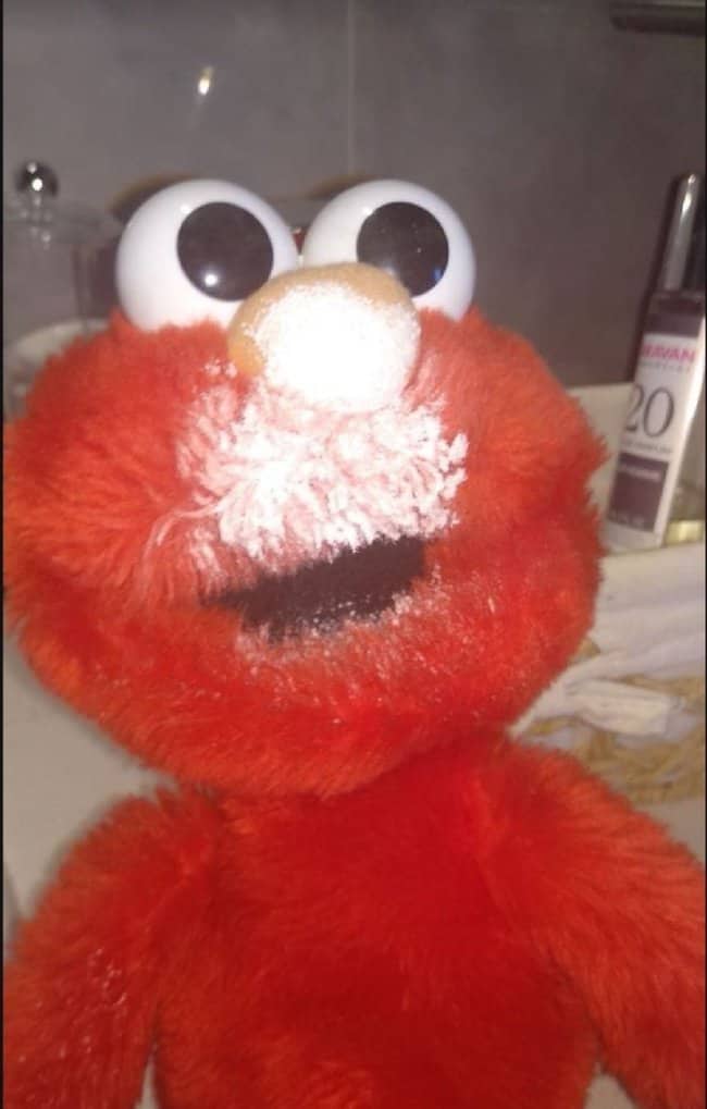 Elmo plush with white powder covering its nose and mouth next to a bathroom counter