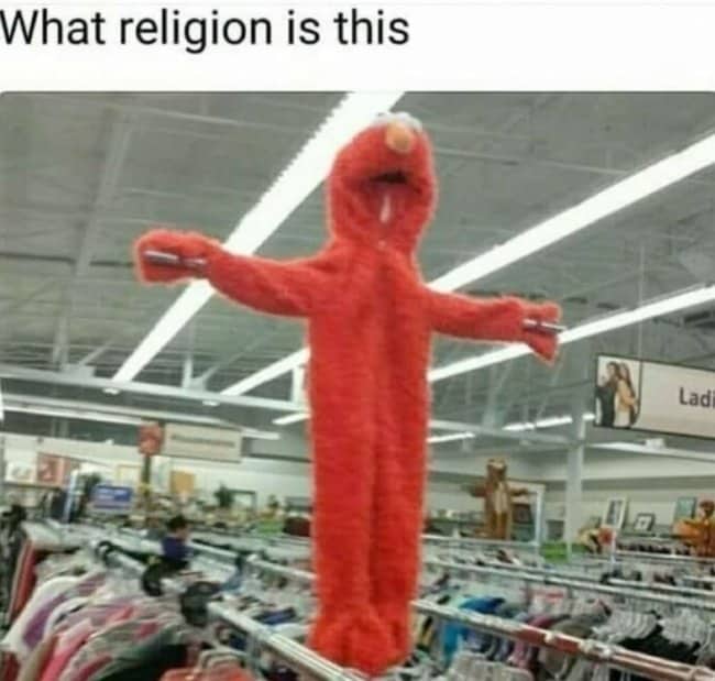 Elmo costume hung with arms outstretched above thrift store clothing racks, asking what religion this is