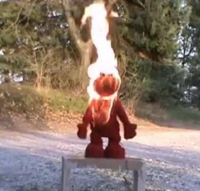 Elmo doll bursting into smoke and flames on a wooden bench outdoors