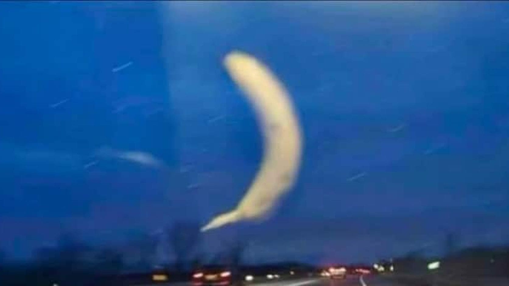 A banana stuck to a car windshield at dusk looks like a glowing crescent moon over the highway, from today's relatable memes.